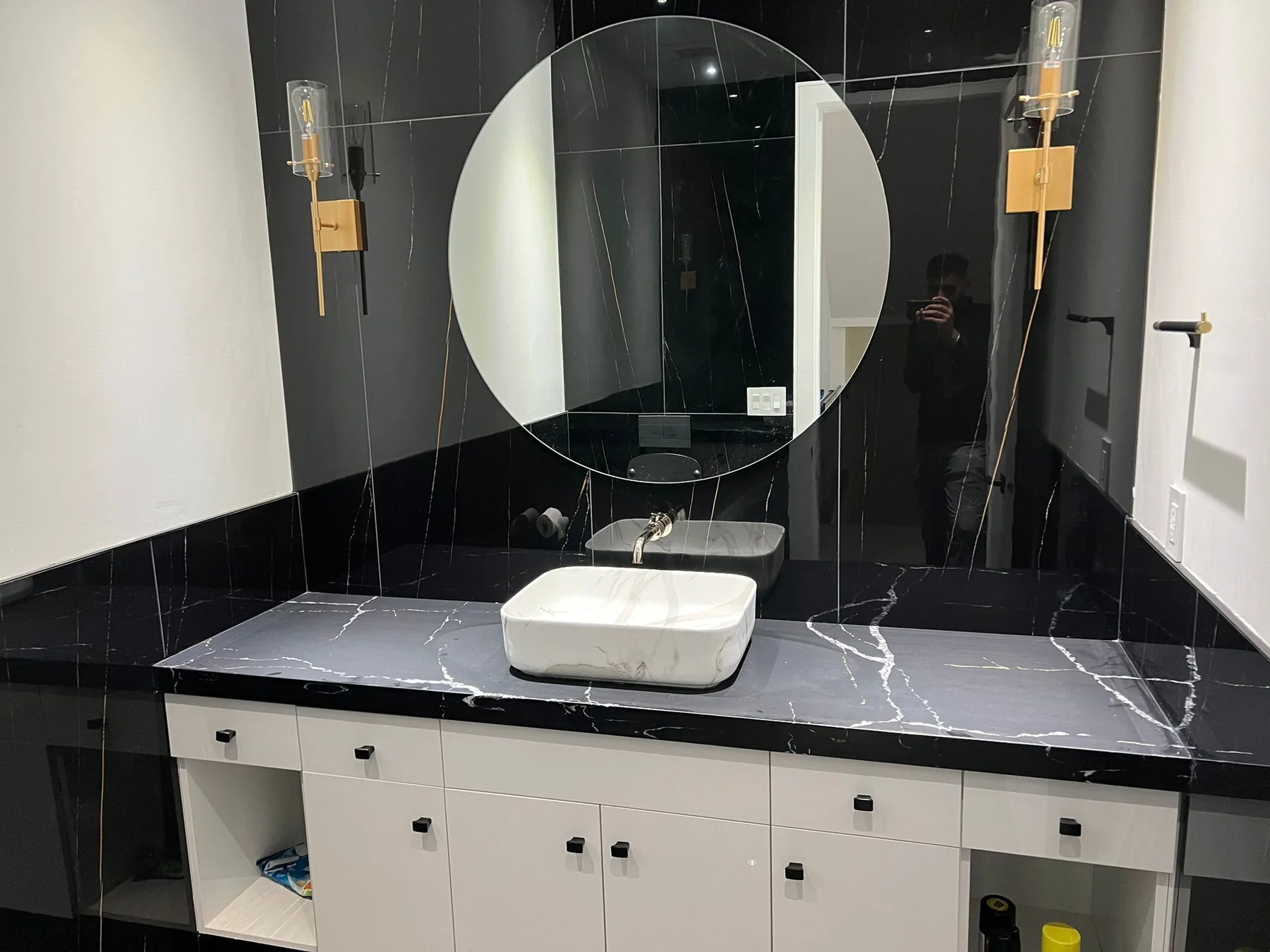 Black bathroom vanity with stone wall and round mirror.
