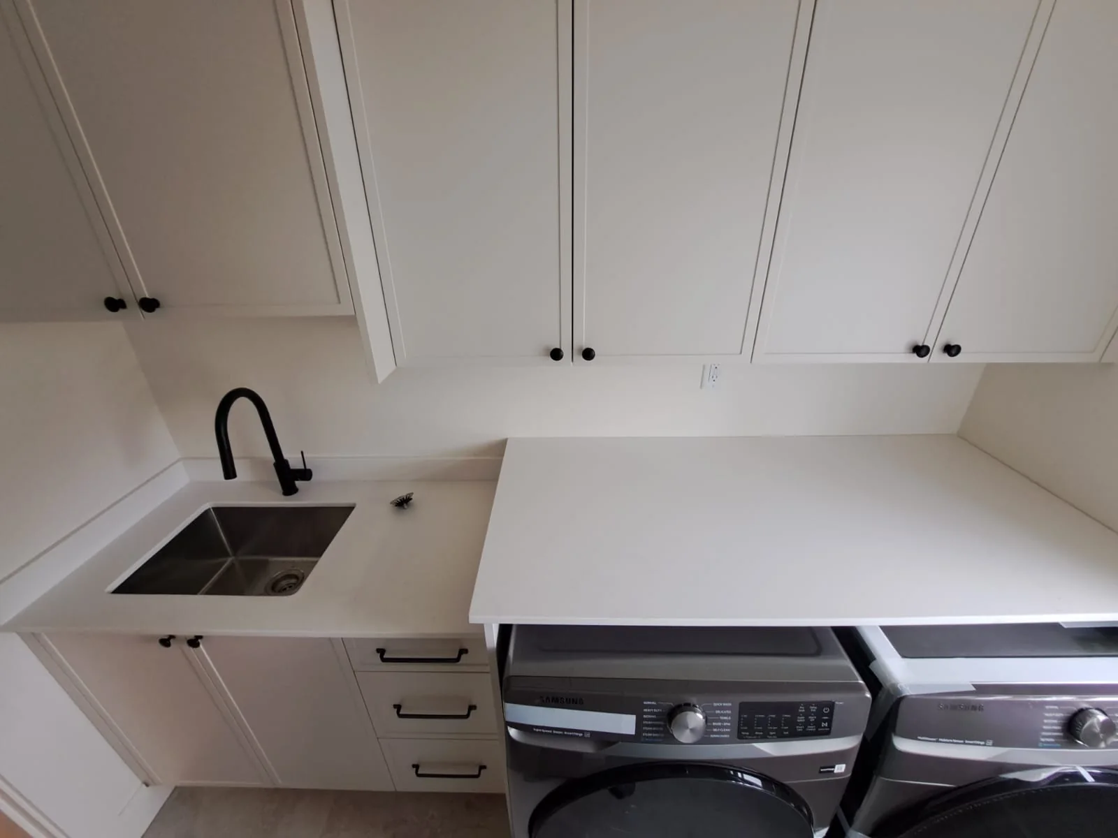 Compact kitchen with white countertop and black fixtures.