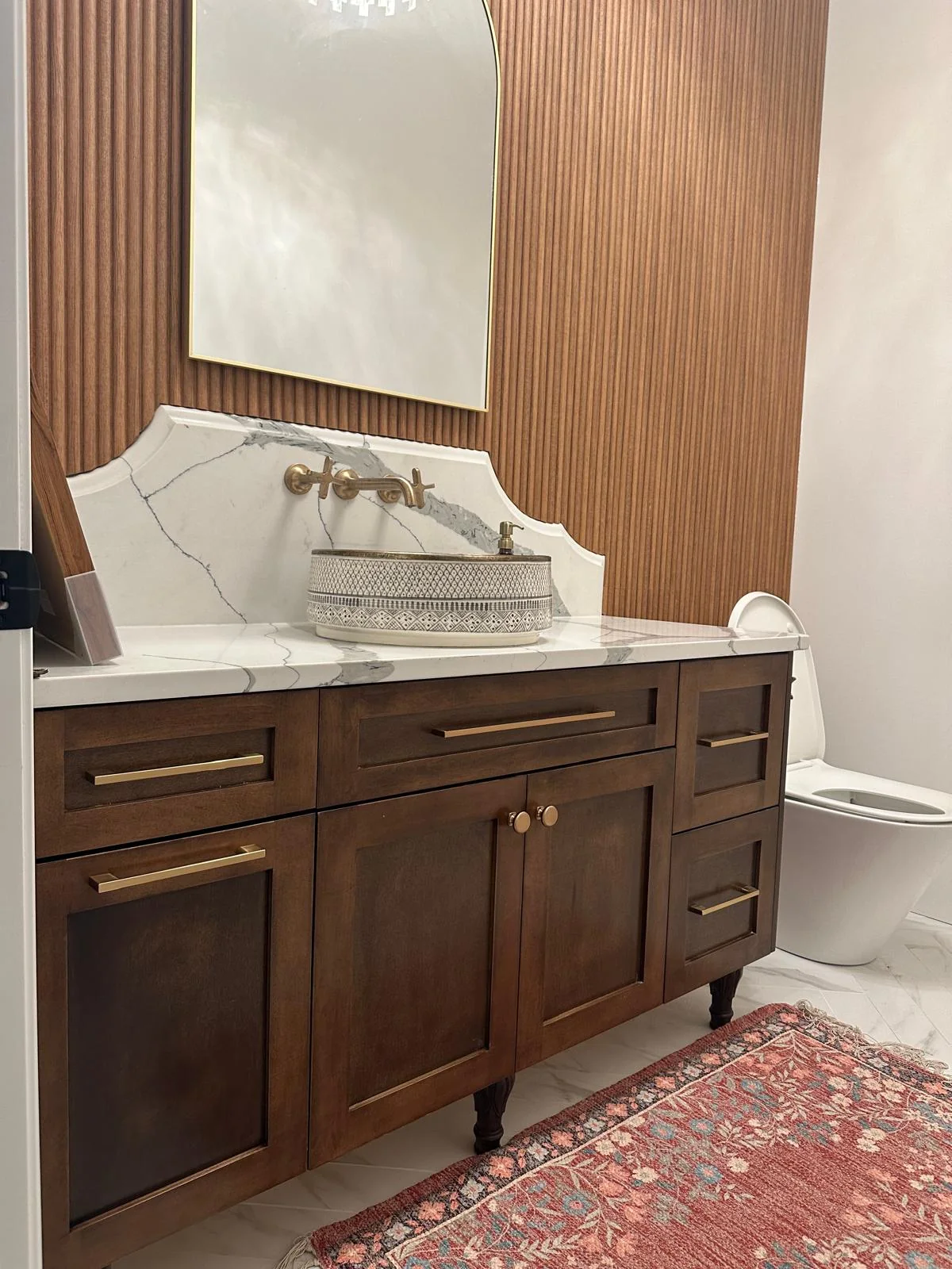 Wood bathroom vanity with stone countertop and mirror.